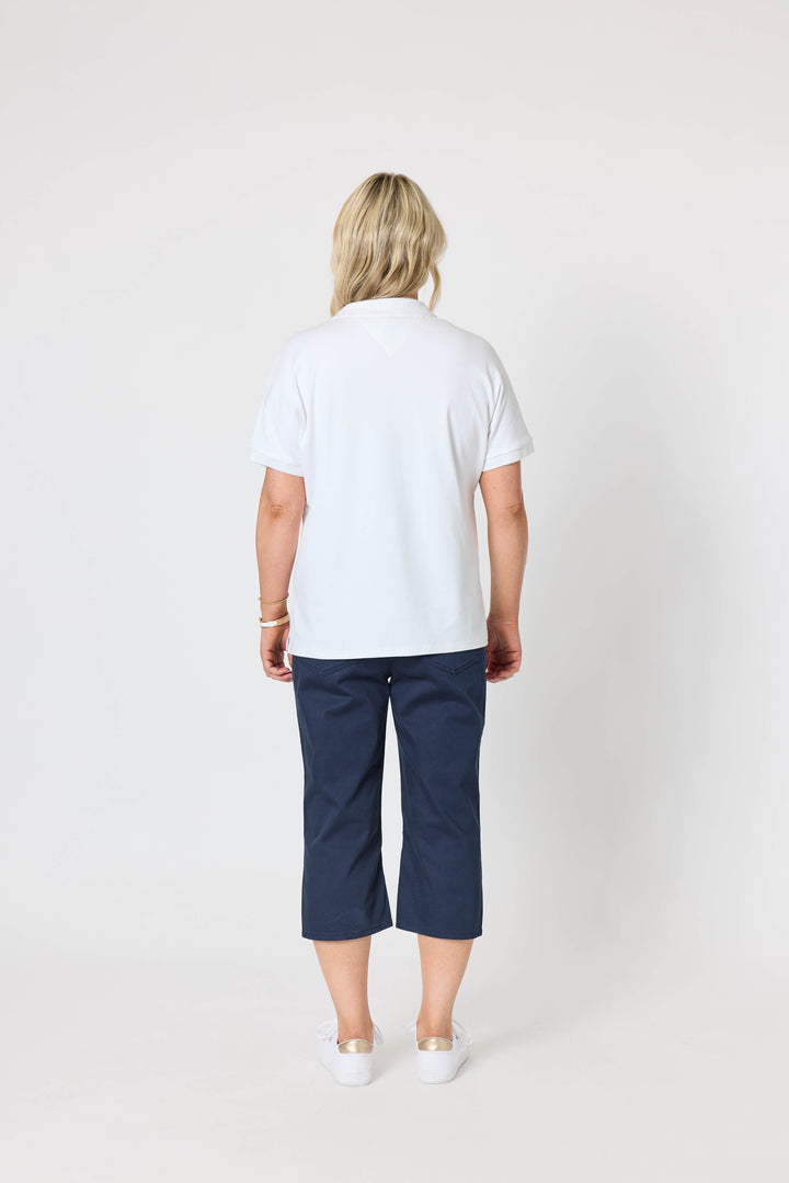 Gordon Smith Model A woman modeling a white short-sleeve polo shirt and navy blue cropped pants against a plain light gray studio background.
