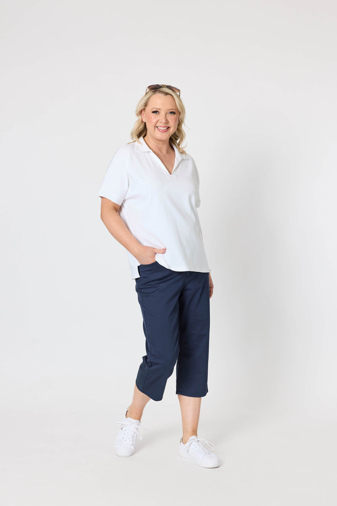 Gordon Smith Model A woman modeling a white short-sleeve polo shirt and navy blue cropped pants against a plain light gray studio background.
