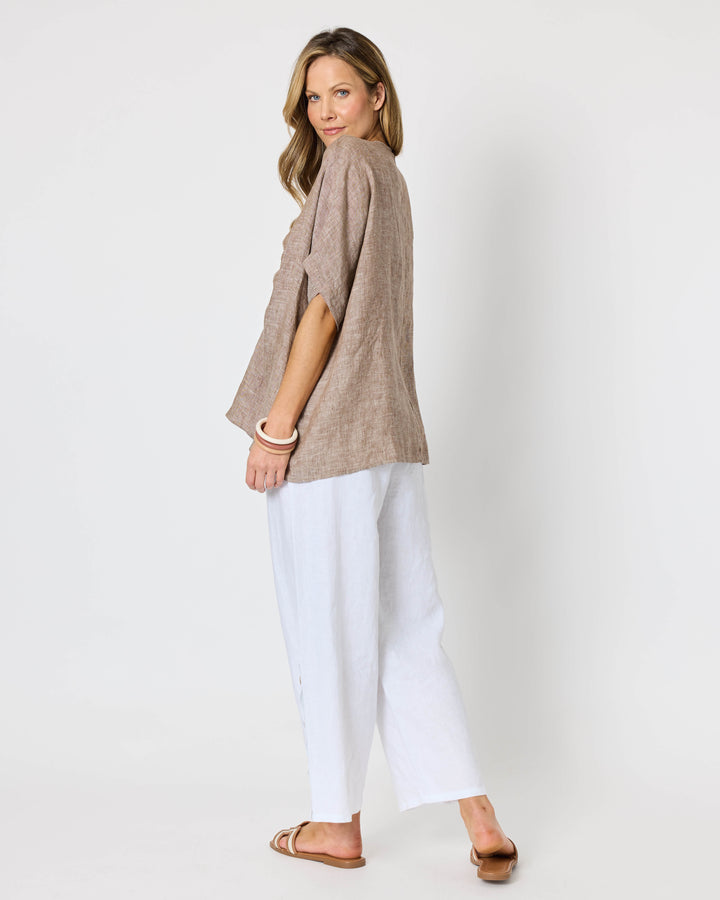 A Hammock &amp; Vine model wearing a loose taupe knit wrap top with a front knot detail, paired with white wide-leg cropped pants and tan sandals, against a plain white studio background.