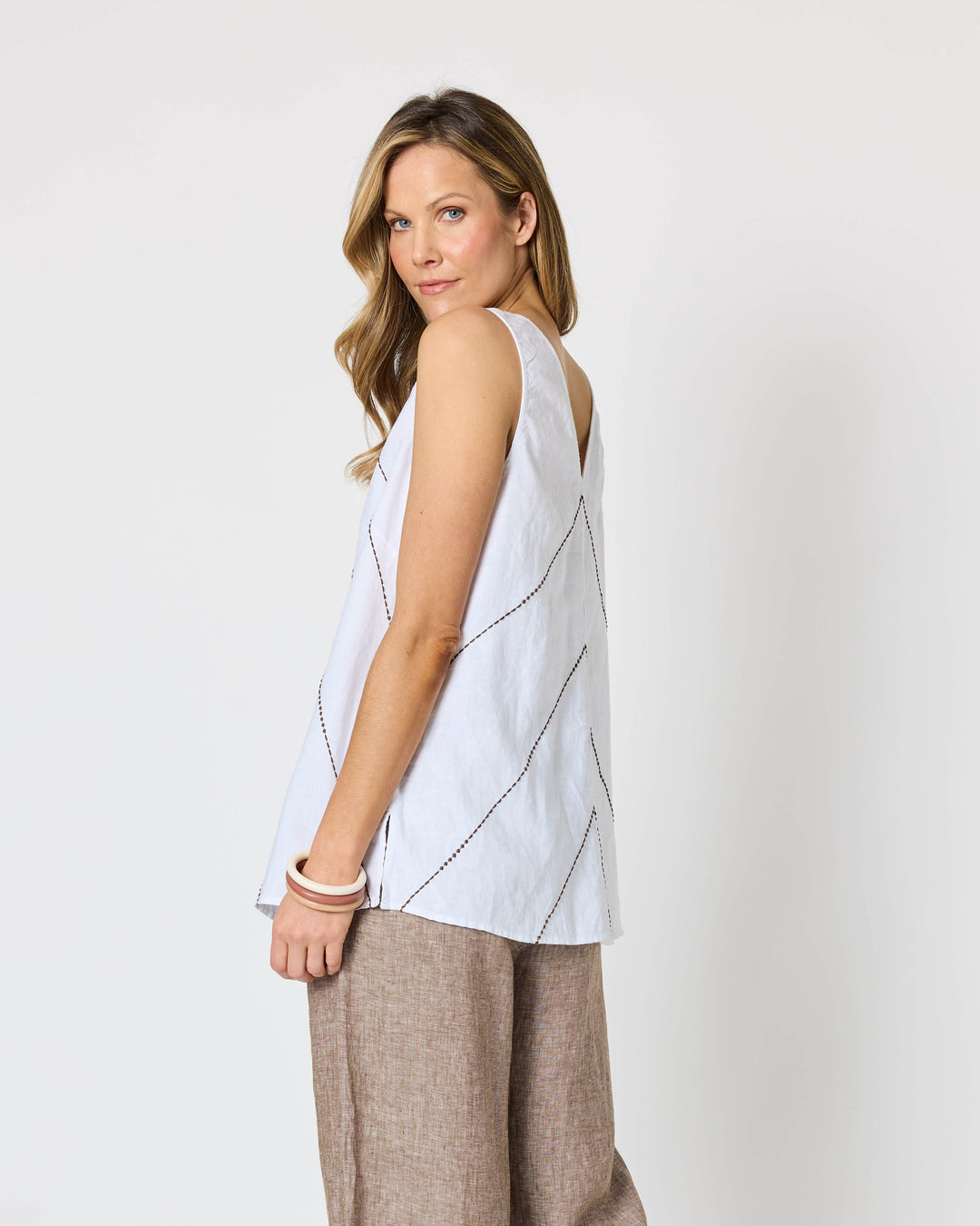 A Hammock &amp; Vine model wearing a sleeveless white top with thin brown line details and wide-leg taupe pants against a plain white studio background.
