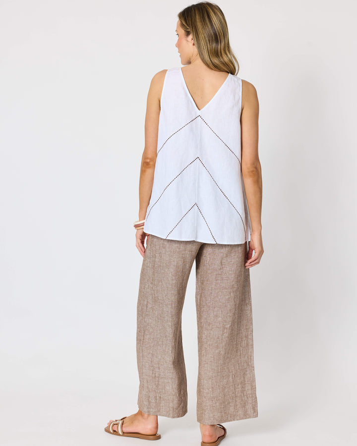 A hammock &amp; vine model shown from the back wearing a sleeveless white top with a V-neckline and geometric line pattern, paired with wide-leg taupe pants and flat sandals, against a plain white studio background.
