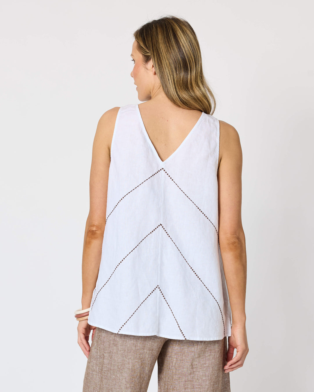 A Hammock &amp; Vine model seen from the back wearing a sleeveless white top with a V-neckline and geometric line pattern, paired with wide-leg taupe pants and flat sandals, against a plain white studio background.