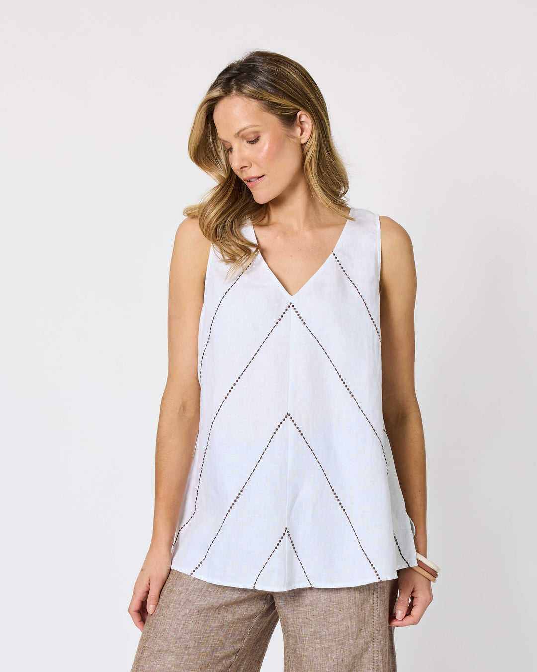 A Hammock &amp; Vine model wearing a sleeveless white top with thin brown line details and wide-leg taupe pants against a plain white studio background.
