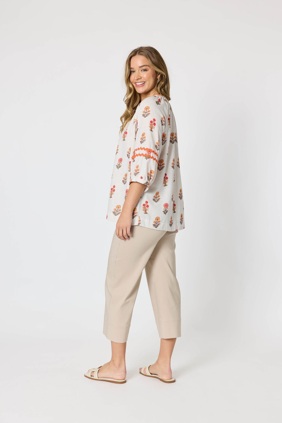 Threadz woman modeling a white button-up blouse with a colorful floral and geometric print, paired with coral-colored cropped pants and flat sandals, against a plain white studio background.