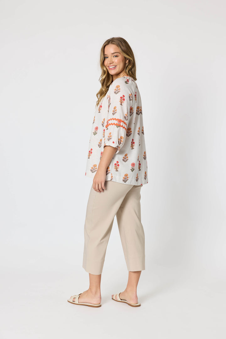 Threadz woman modeling a white button-up blouse with a colorful floral and geometric print, paired with coral-colored cropped pants and flat sandals, against a plain white studio background.