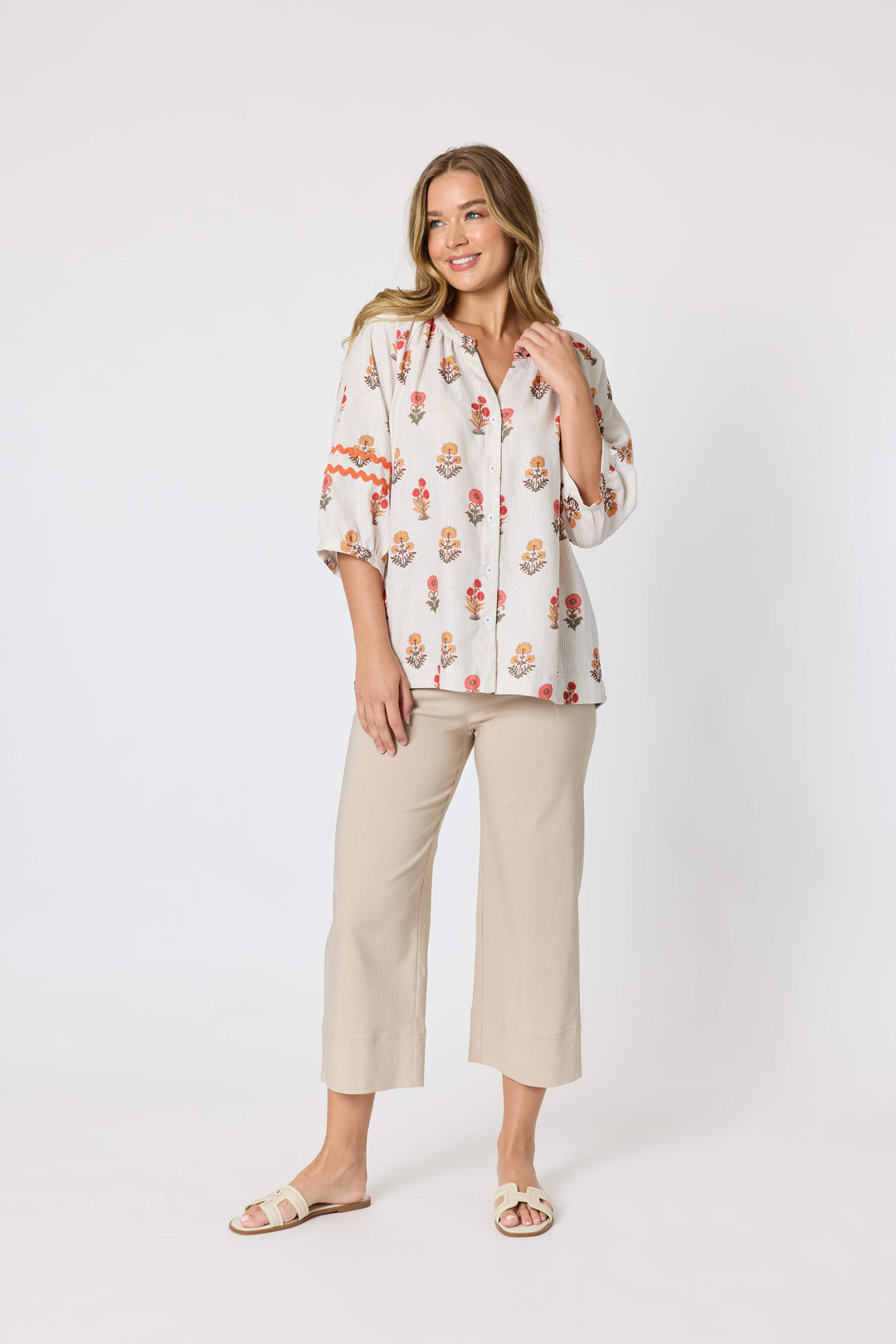 Threadz woman modeling a white button-up blouse with a colorful floral and geometric print, paired with coral-colored cropped pants and flat sandals, against a plain white studio background.
