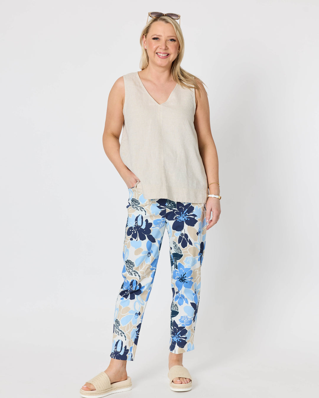 Gordon Smith  woman modeling a sleeveless light beige top and blue floral print pants with cream slide sandals, standing against a plain light gray studio background.