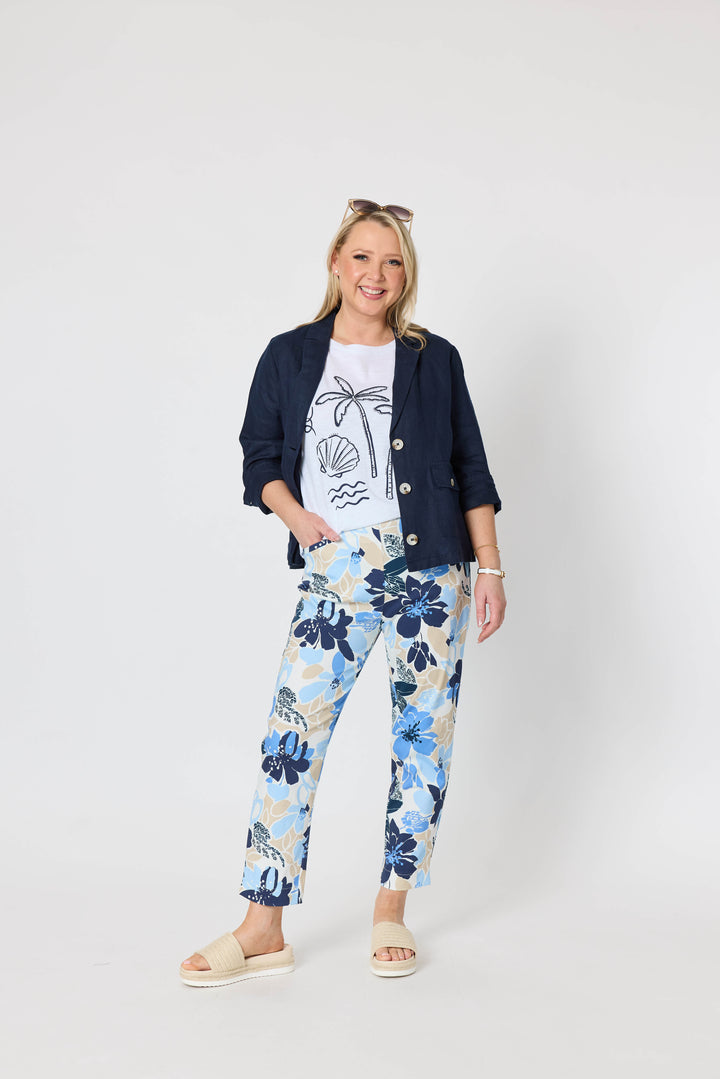 Gordon Smith  woman modeling a sleeveless light beige top and blue floral print pants with cream slide sandals, standing against a plain light gray studio background.
