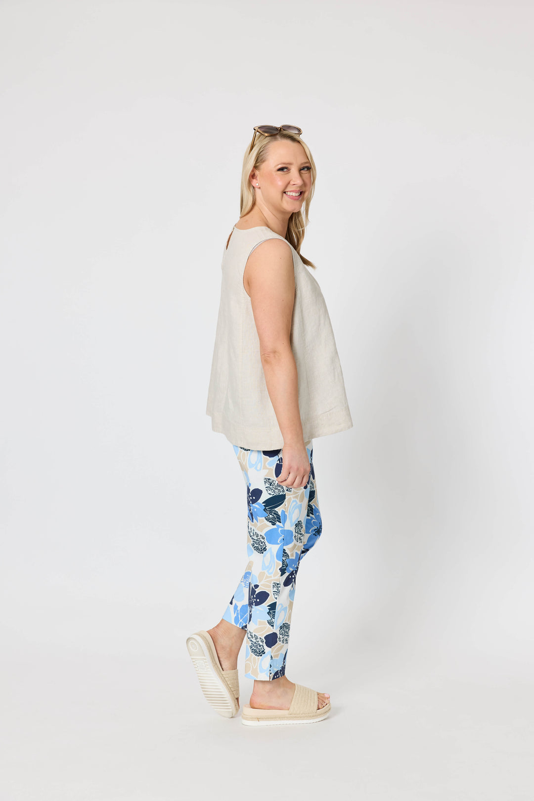 Gordon Smith  woman modeling a sleeveless light beige top and blue floral print pants with cream slide sandals, standing against a plain light gray studio background.