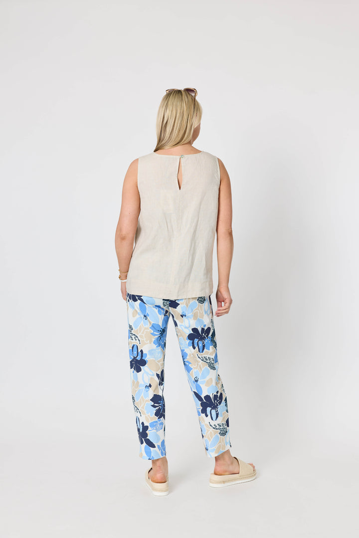 Gordon Smith  woman modeling a sleeveless light beige top and blue floral print pants with cream slide sandals, standing against a plain light gray studio background. Back view