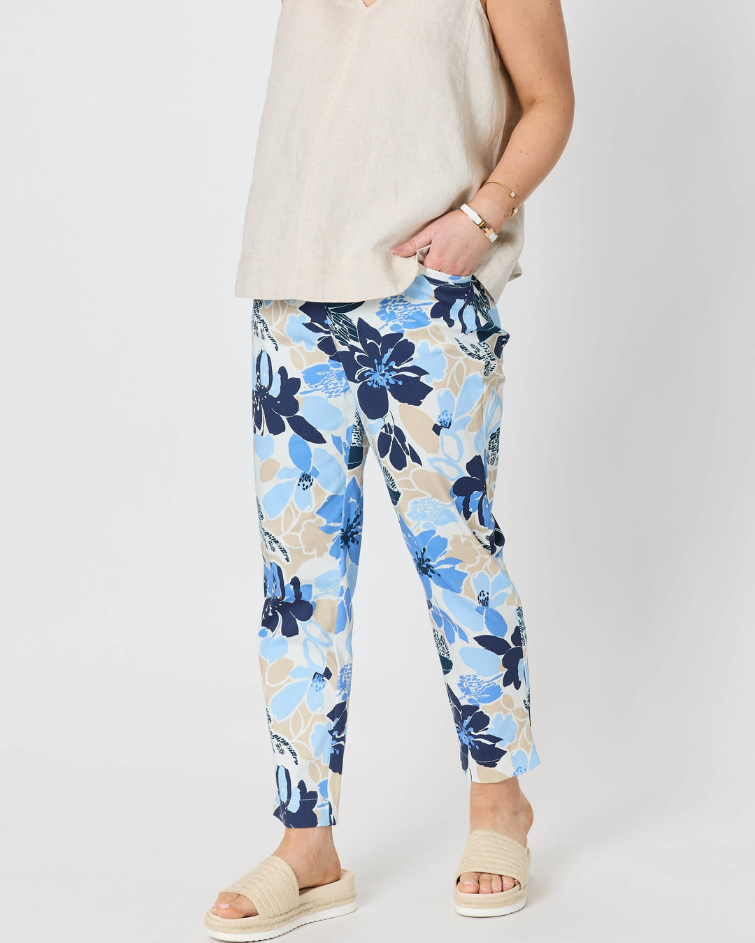 Gordon Smith  woman modeling a sleeveless light beige top and blue floral print pants with cream slide sandals, standing against a plain light gray studio background.