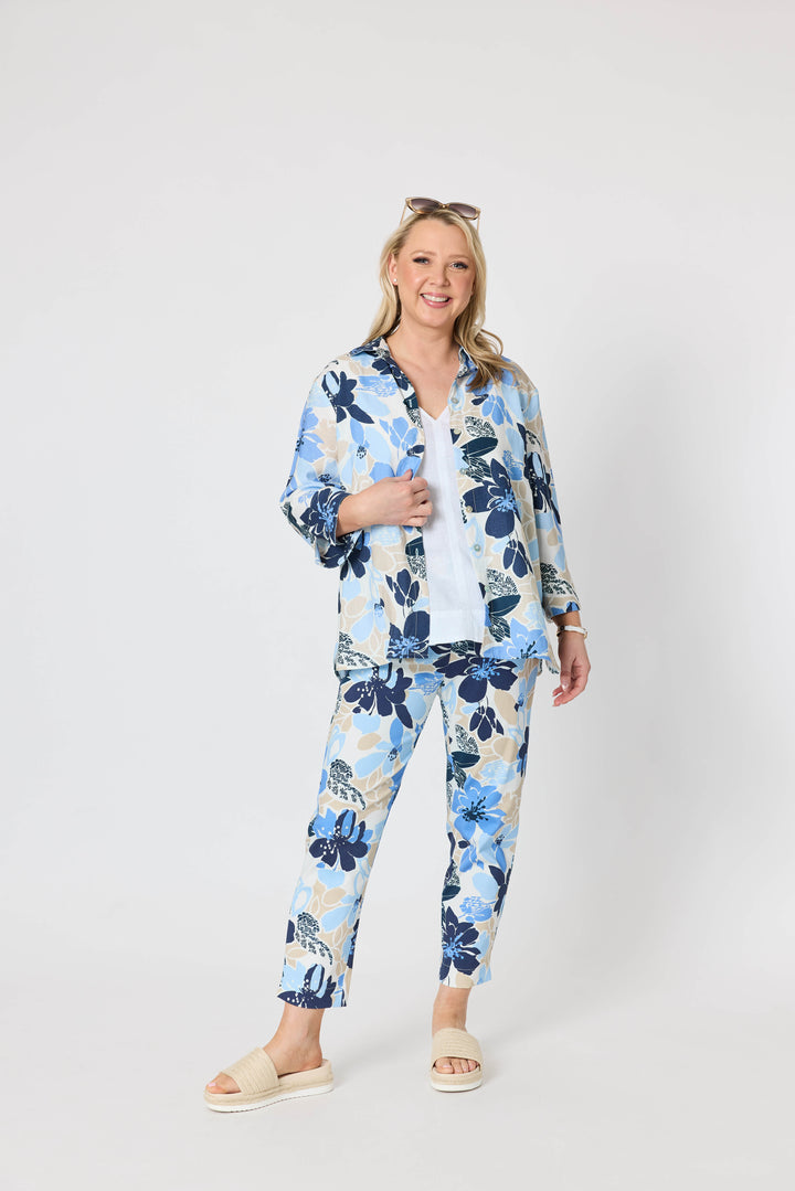 Gordon Smith  woman modeling a sleeveless light beige top and blue floral print pants with cream slide sandals, standing against a plain light gray studio background.