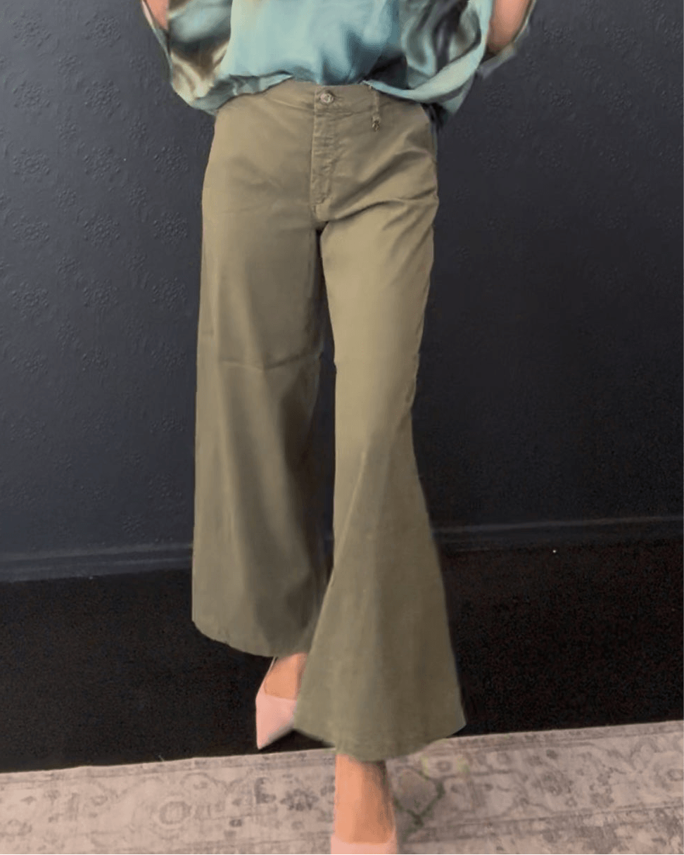 Mos Mosh A model wearing olive green wide-leg cropped flare pants with a matching top, standing against a dark textured wall.