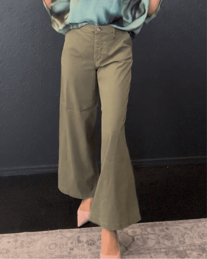 Mos Mosh A model wearing olive green wide-leg cropped flare pants with a matching top, standing against a dark textured wall.