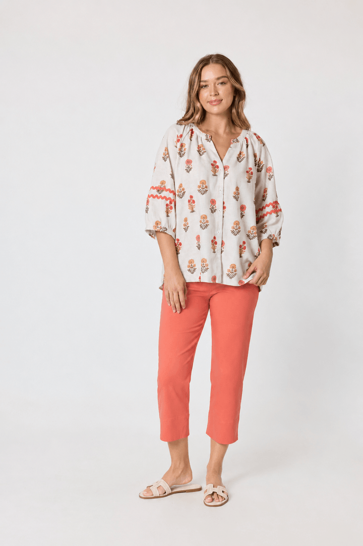 Threadz woman modeling a white V-neck short-sleeve t-shirt and coral orange cropped pants, paired with white sneakers, against a plain light gray studio background.