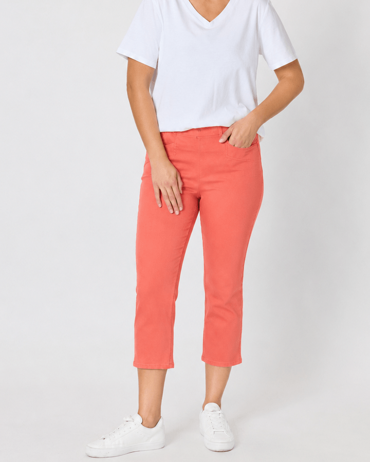 Threadz woman modeling a white V-neck short-sleeve t-shirt and coral orange cropped pants, paired with white sneakers, against a plain light gray studio background.
