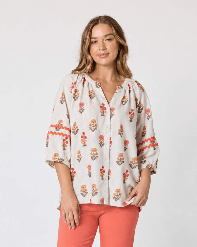 Threadz woman modeling a white button-up blouse with a colorful floral and geometric print, paired with coral-colored cropped pants and flat sandals, against a plain white studio background.