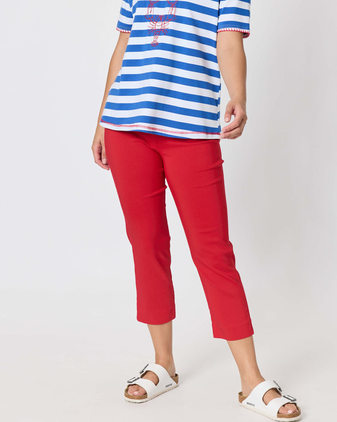 Threadz. A woman modeling a short-sleeve blue and white striped t-shirt with red trim and a red graphic print, paired with red cropped pants and white slide sandals, against a plain white studio background.
