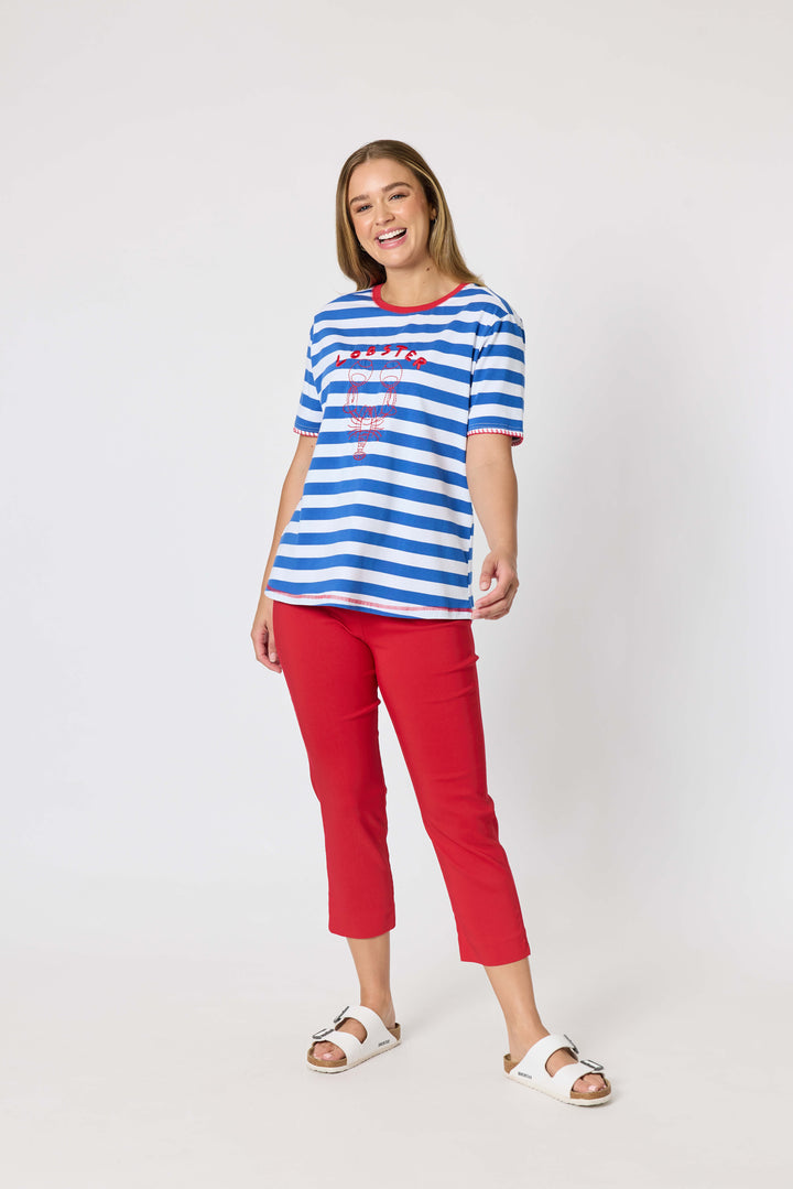 Threadz. A woman modeling a short-sleeve blue and white striped t-shirt with red trim and a red graphic print, paired with red cropped pants and white slide sandals, against a plain white studio background.