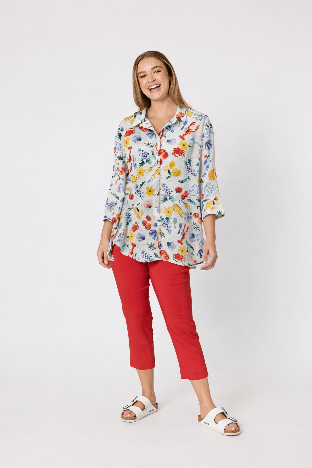 Threadz. A woman modeling a short-sleeve blue and white striped t-shirt with red trim and a red graphic print, paired with red cropped pants and white slide sandals, against a plain white studio background.