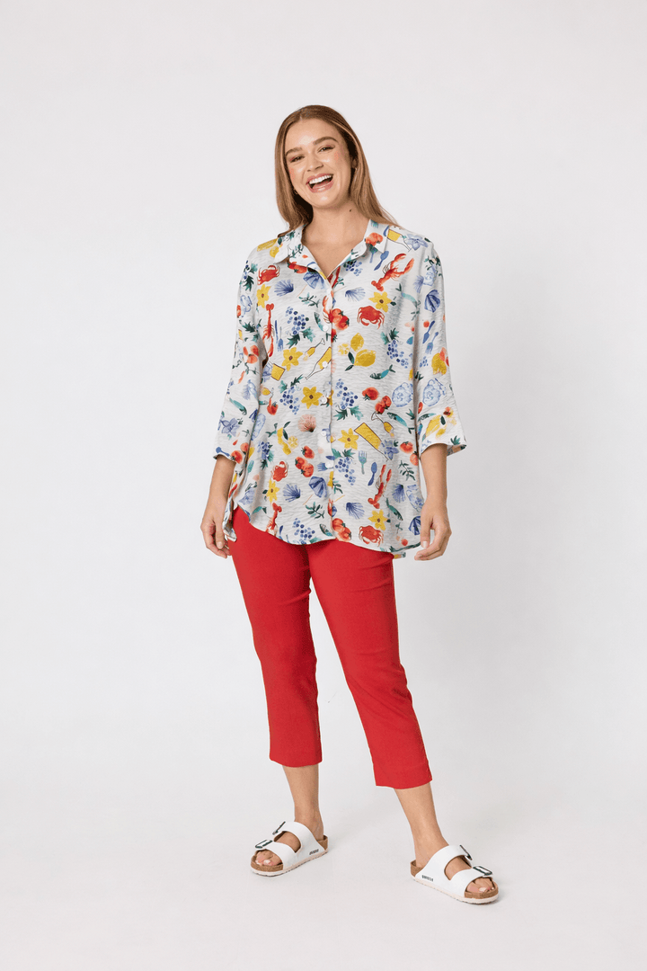 Threadz. A woman modeling a short-sleeve blue and white striped t-shirt with red trim and a red graphic print, paired with red cropped pants and white slide sandals, against a plain white studio background.