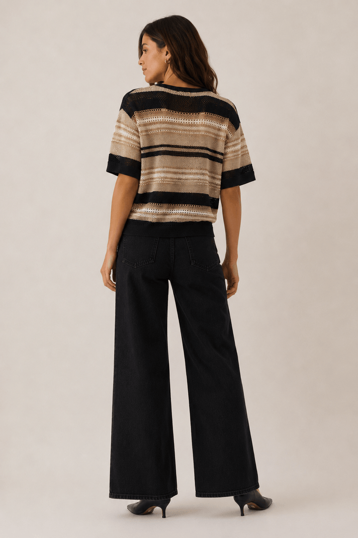 LD&amp;Co modeling wearing a short-sleeve knit sweater with horizontal beige, brown, and black stripes, paired with black jeans, against a plain light beige studio background back view 