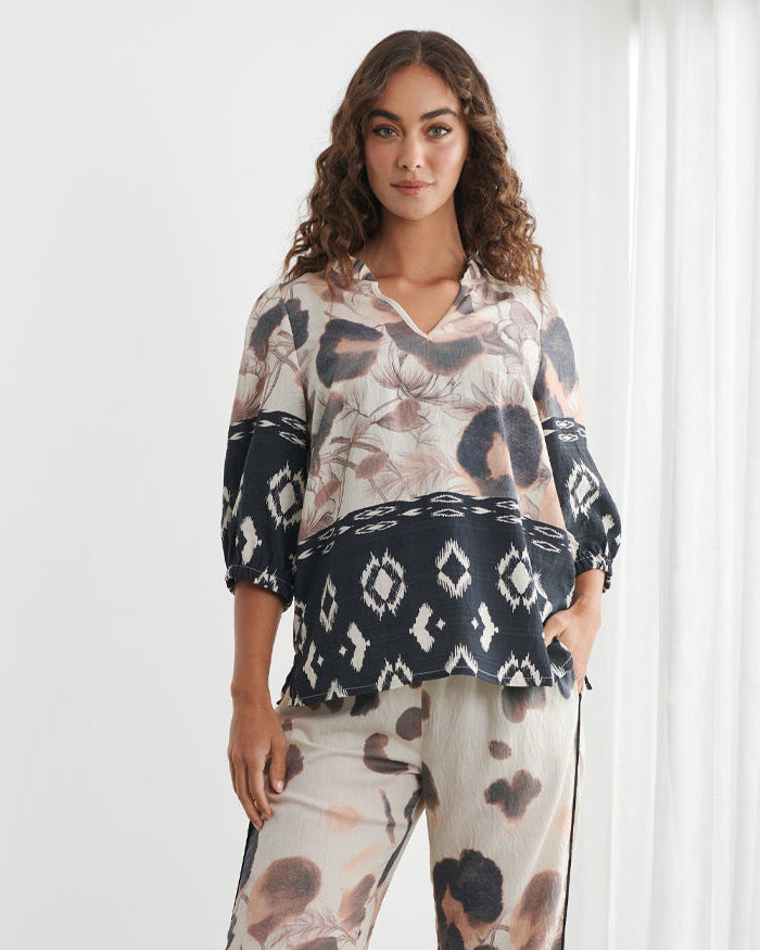 Caju models a matching two-piece lounge set featuring a beige, black, and brown animal print with black geometric lace trim, set against a bright white room with sheer curtains.