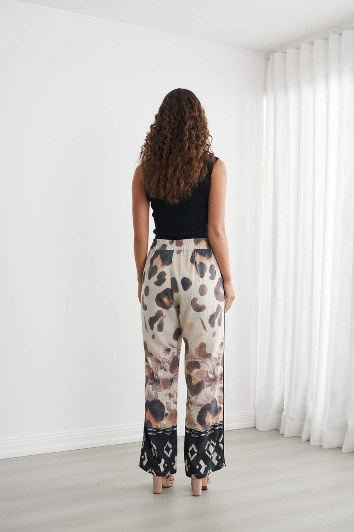 Caju modeling wide-leg pants with a beige, brown, and black abstract pattern, paired with a black tank top and neutral sandals, standing in a bright room with white walls and sheer curtains.
Back view 