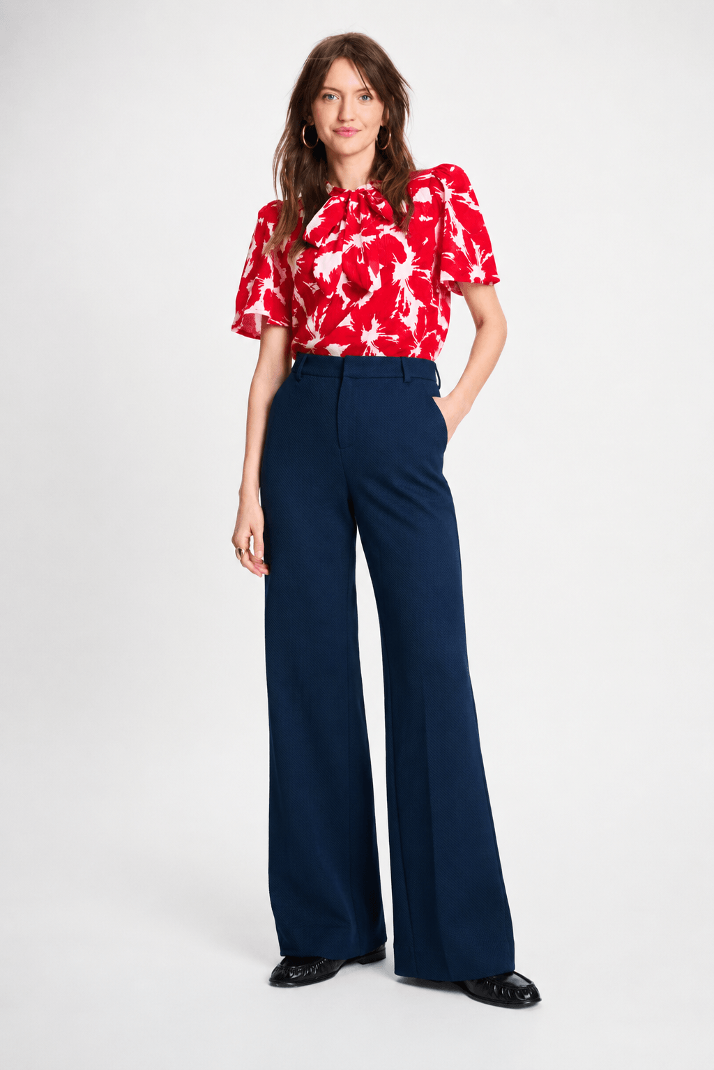 Pom Amsterdam model wearing navy blue wide-leg trousers with a red top partially visible, photographed against a clean white studio background.