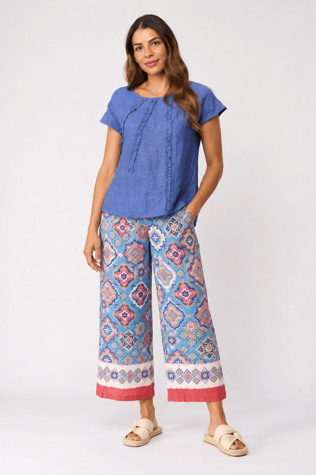 Foil clothing model a sleeveless blue top and wide-leg cropped pants with a colorful geometric pattern in shades of blue, pink, and orange, paired with beige slide sandals, against a light gray studio background.