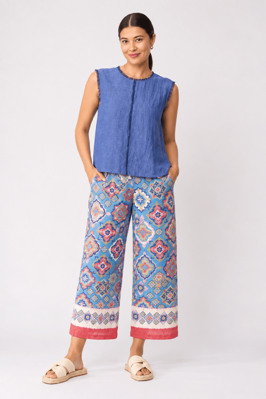 Foil clothing model a sleeveless blue top and wide-leg cropped pants with a colorful geometric pattern in shades of blue, pink, and orange, paired with beige slide sandals, against a light gray studio background.