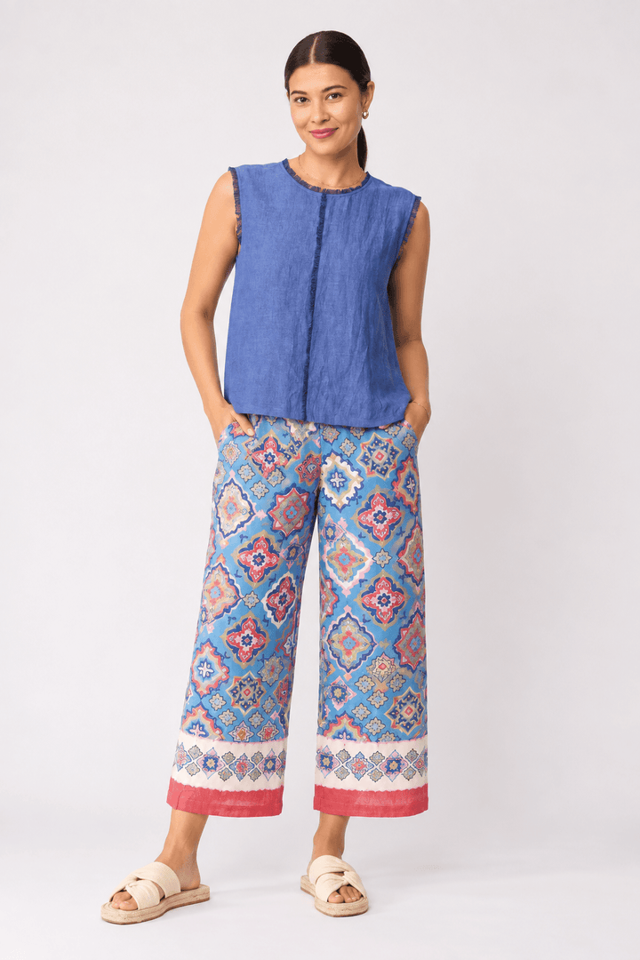 Foil clothing model a sleeveless blue top and wide-leg cropped pants with a colorful geometric pattern in shades of blue, pink, and orange, paired with beige slide sandals, against a light gray studio background.