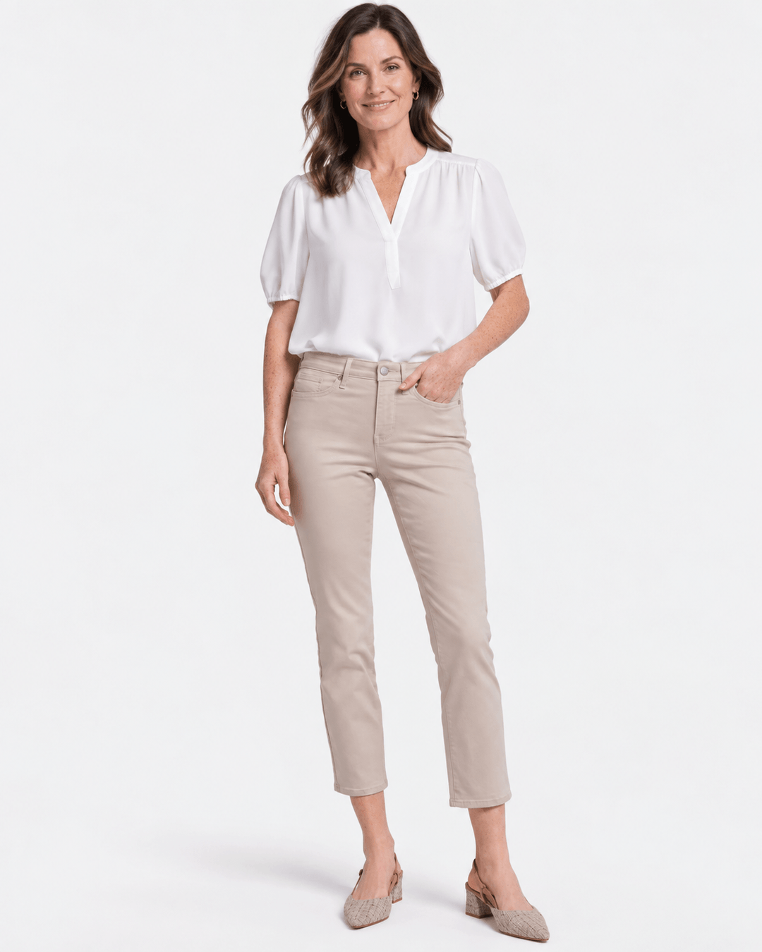 NYDJ modeliin  a white short-sleeve blouse and beige feathers colour cropped pants against a clean white studio background.
