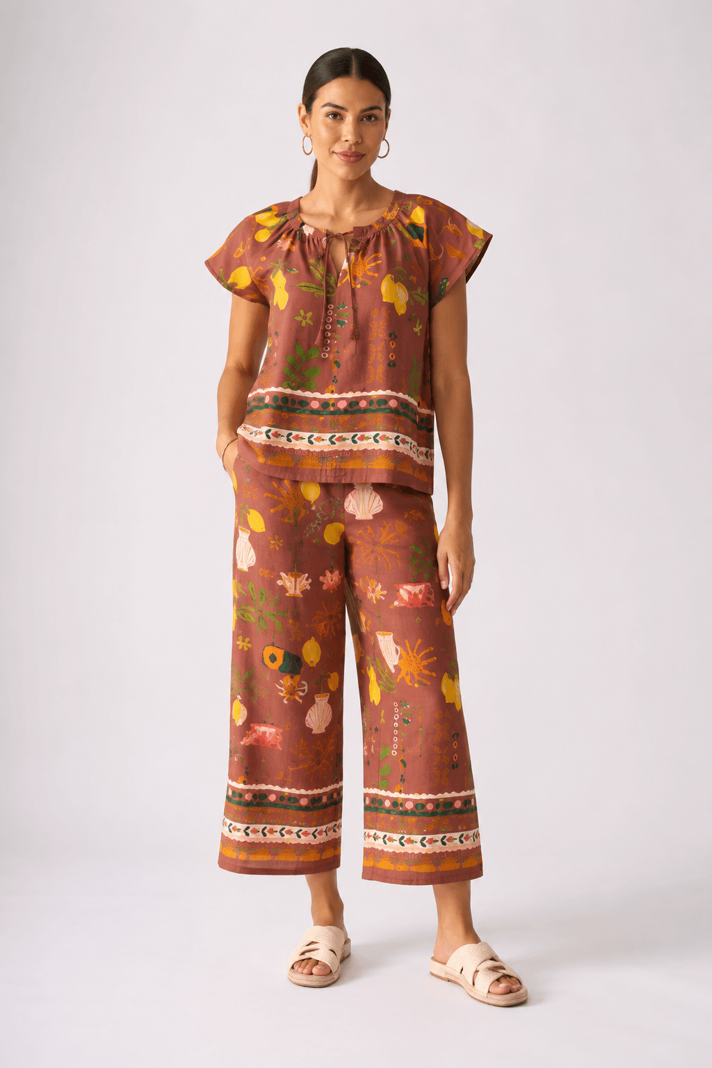Foil Clothing, modeling a short-sleeve top with a brown, orange, and yellow patterned print, paired with light blue wide-leg jeans and brown sandals, against a plain light gray background.