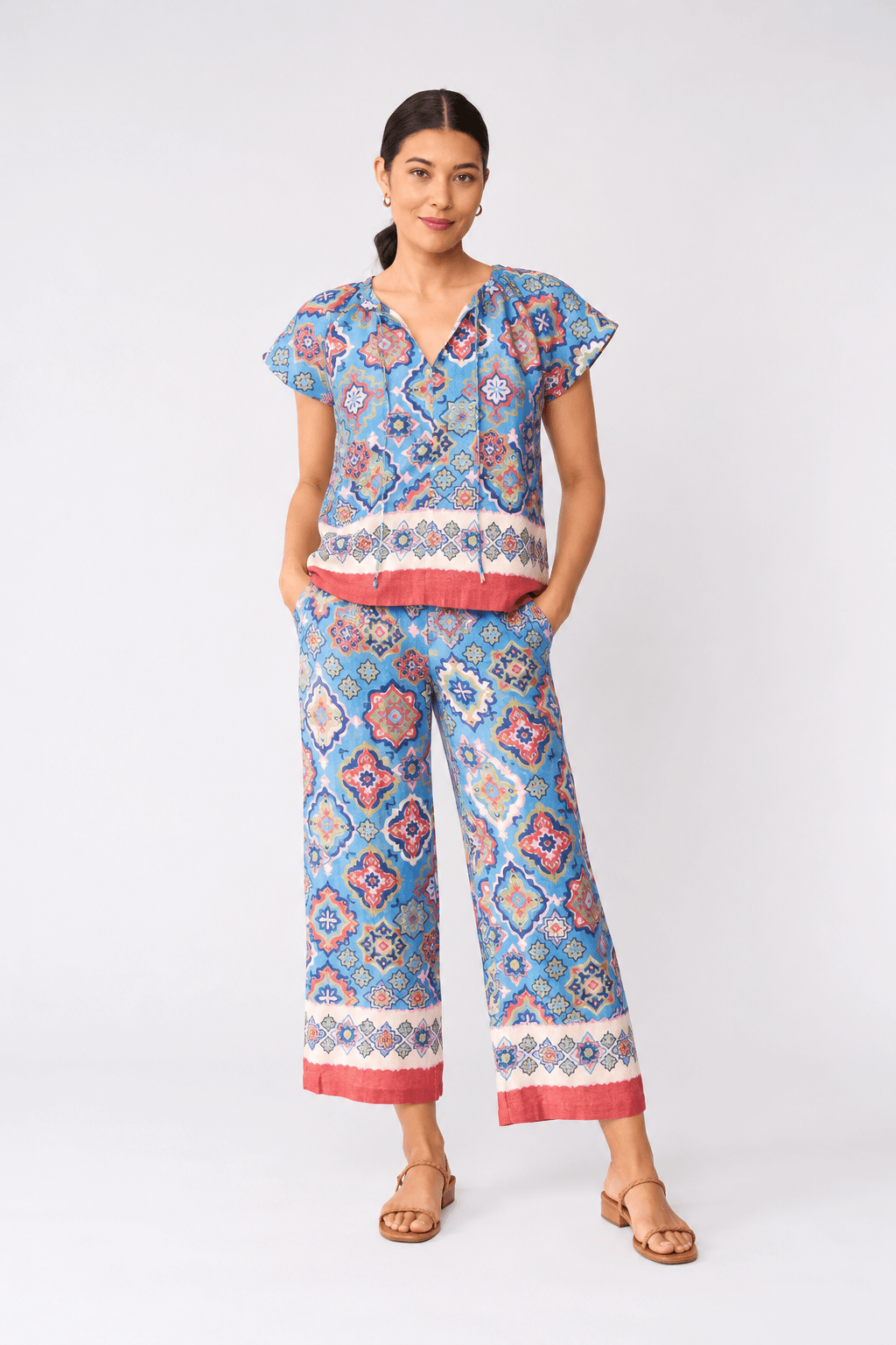Foil modeling a sleeveless matching set of cropped tank top and wide-leg pants with a colorful geometric pattern in blue, pink, and white, paired with beige slide sandals, against a light gray studio background.