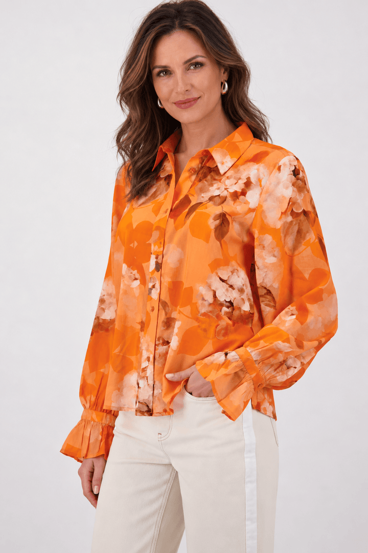 Monari orange tie-dye button-up blouse with pointed collar and long ruffle cuffs on a model. On white studio background.background