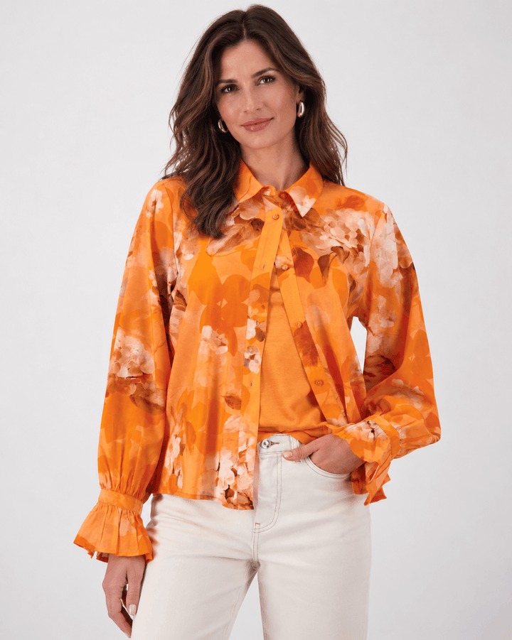 Monari orange tie-dye button-up blouse with pointed collar and long ruffle cuffs on a model. On white studio background.background