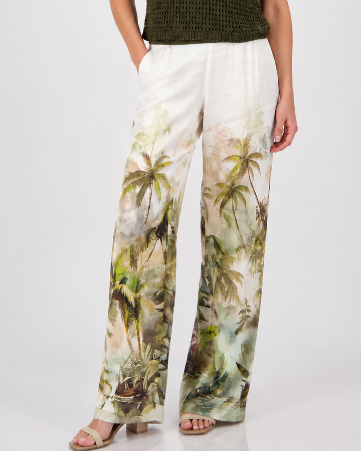 Monari woman modeling a short-sleeve olive green knit top paired with white wide-leg pants featuring a green palm tree print, set against a plain light gray studio background.