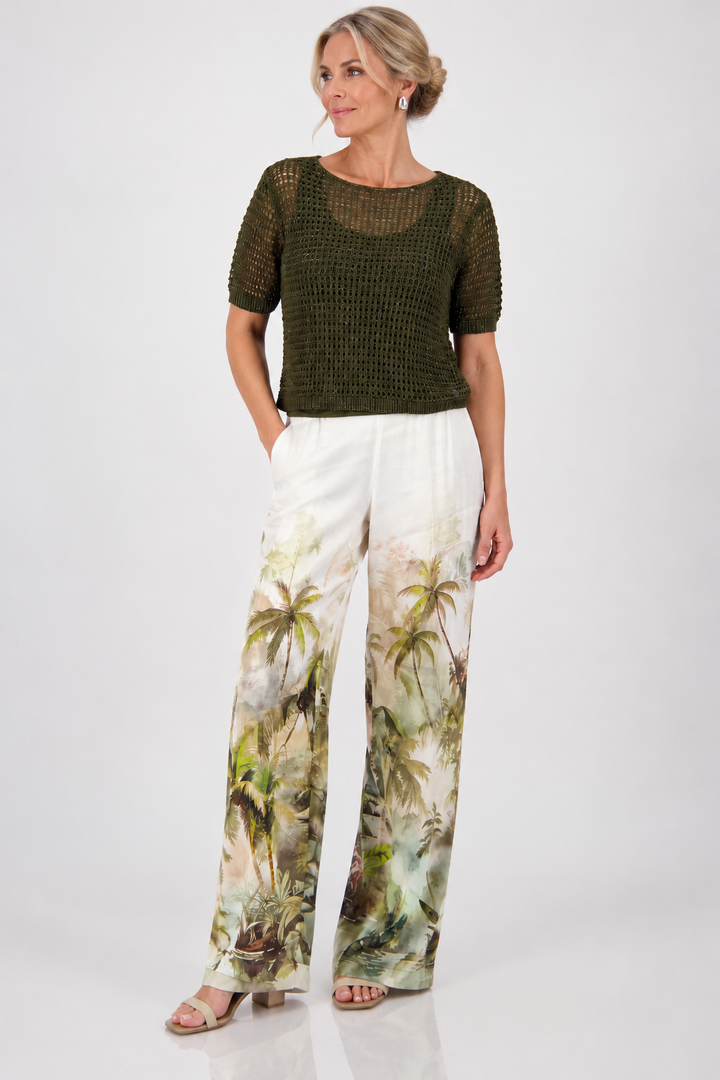 Monari woman modeling a short-sleeve olive green knit top paired with white wide-leg pants featuring a green palm tree print, set against a plain light gray studio background.