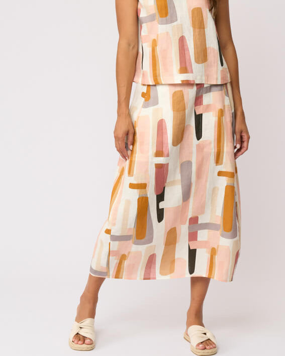 Foil modeling a sleeveless midi dress with a matching belt and skirt, featuring an abstract geometric print in peach, orange, pink, and beige on a white background, set against a plain light gray studio backdrop.