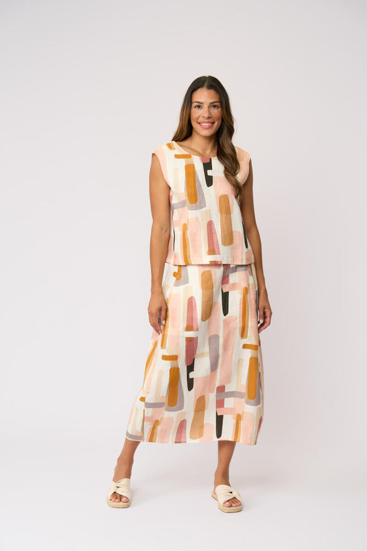 Foil modeling a sleeveless midi dress with a matching belt and skirt, featuring an abstract geometric print in peach, orange, pink, and beige on a white background, set against a plain light gray studio backdrop.