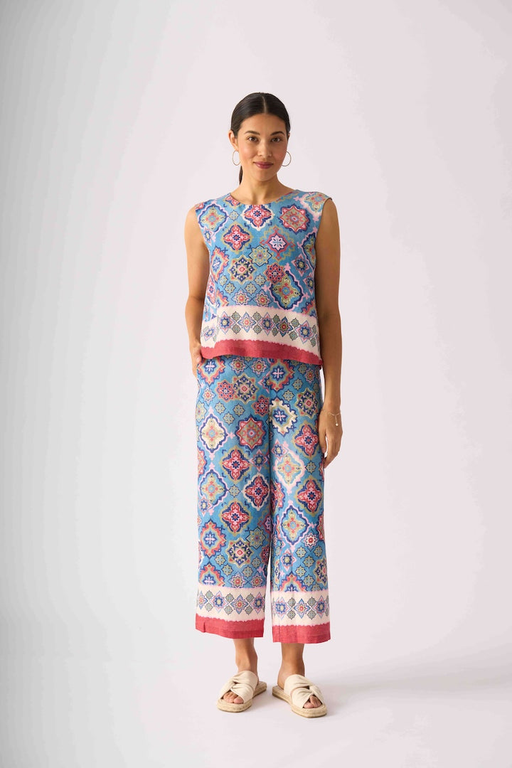 Foil modeling a sleeveless matching set of cropped tank top and wide-leg pants with a colorful geometric pattern in blue, pink, and white, paired with beige slide sandals, against a light gray studio background.