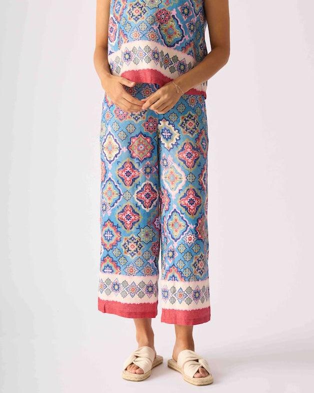 Foil modeling a sleeveless matching set of cropped tank top and wide-leg pants with a colorful geometric pattern in blue, pink, and white, paired with beige slide sandals, against a light gray studio background.