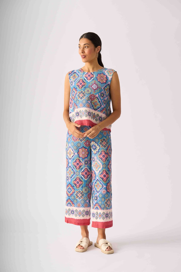 Foil modeling a sleeveless matching set of cropped tank top and wide-leg pants with a colorful geometric pattern in blue, pink, and white, paired with beige slide sandals, against a light gray studio background.
