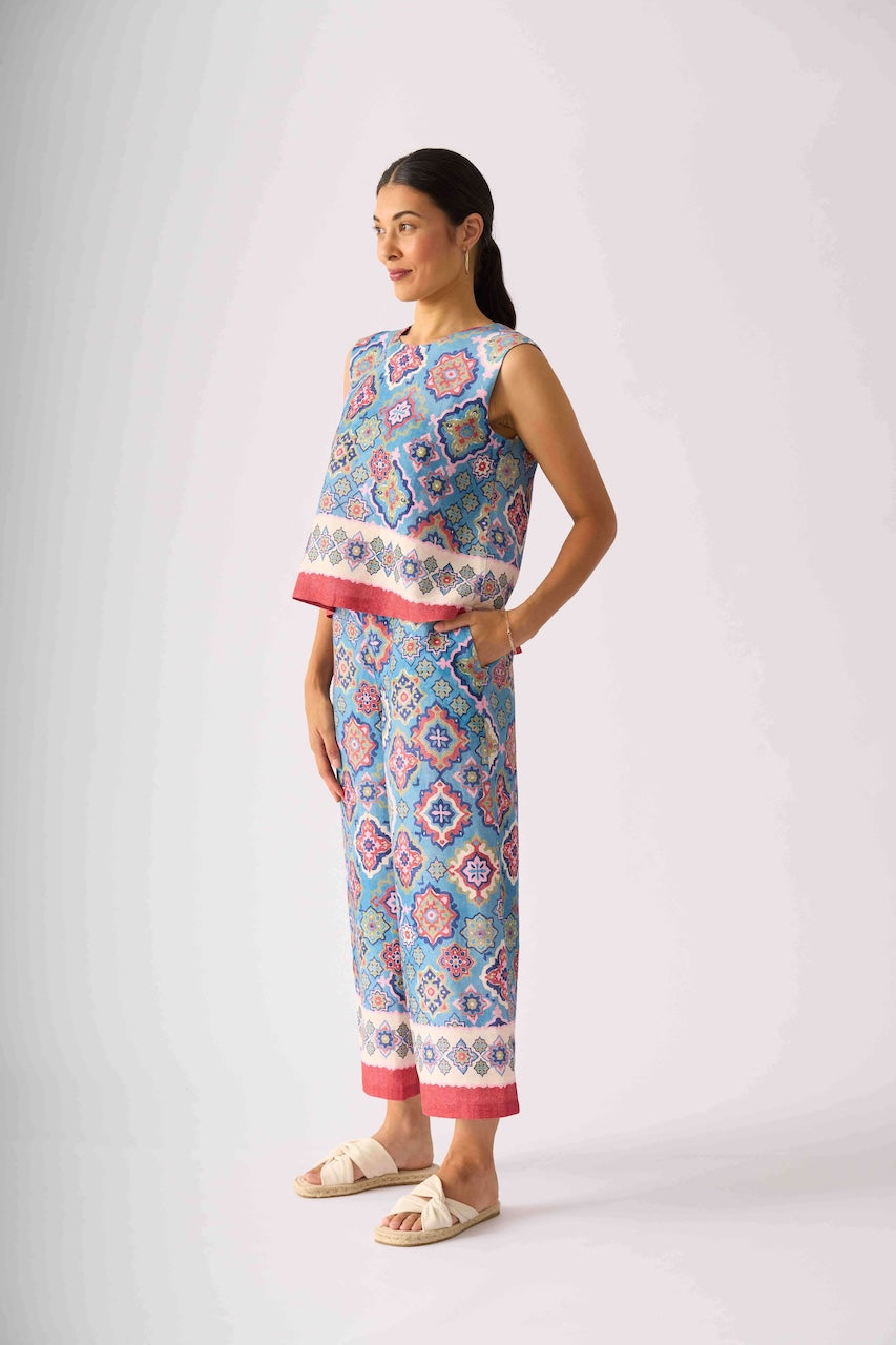 Foil modeling a sleeveless matching set of cropped tank top and wide-leg pants with a colorful geometric pattern in blue, pink, and white, paired with beige slide sandals, against a light gray studio background.
