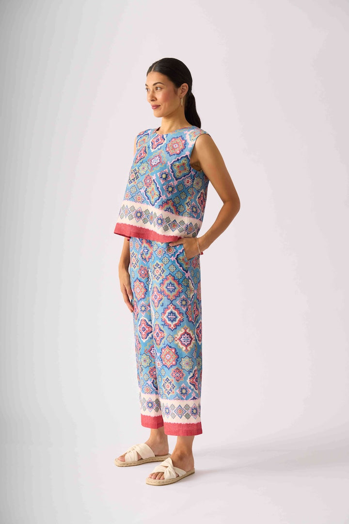 Foil modeling a sleeveless matching set of cropped tank top and wide-leg pants with a colorful geometric pattern in blue, pink, and white, paired with beige slide sandals, against a light gray studio background.