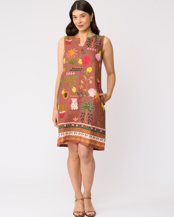 Foil clothing modeling a sleeveless brown dress with a colorful tropical and floral print, standing against a plain white studio background.