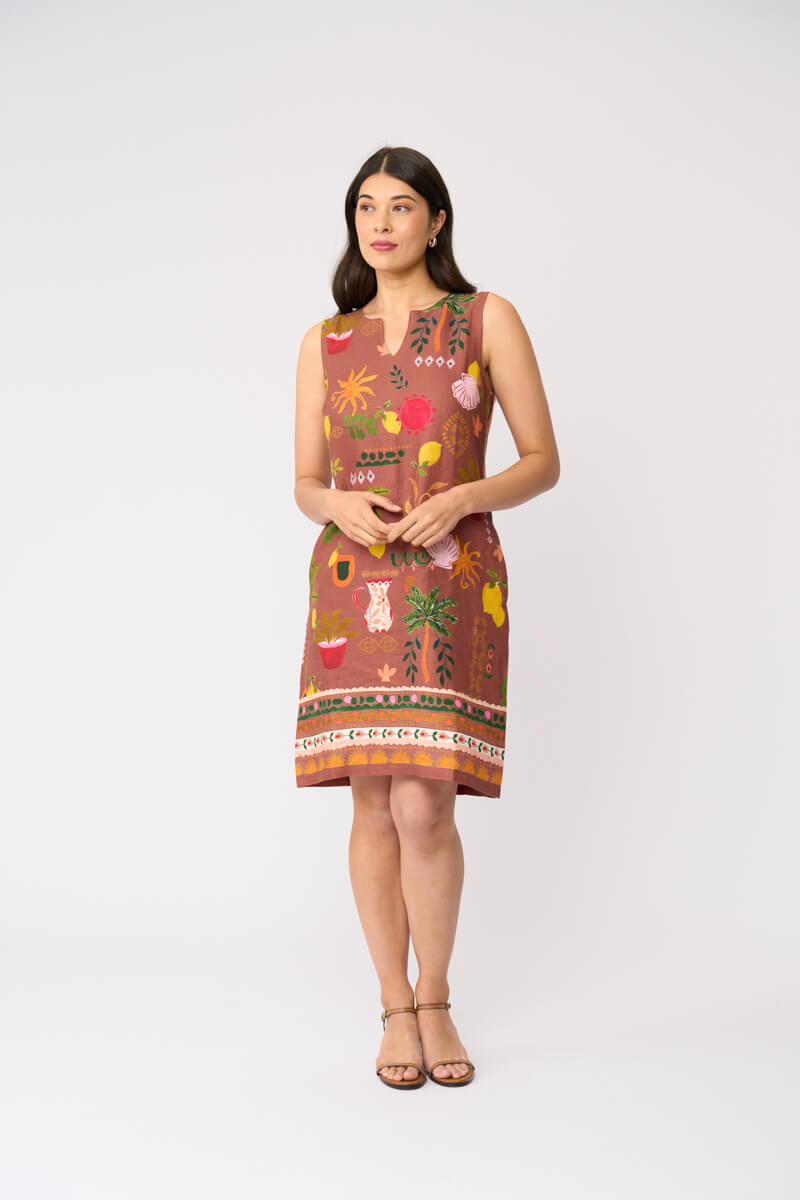Foil clothing modeling a sleeveless brown dress with a colorful tropical and floral print, standing against a plain white studio background.