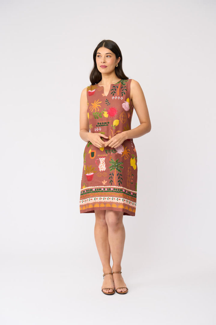 Foil clothing modeling a sleeveless brown dress with a colorful tropical and floral print, standing against a plain white studio background.