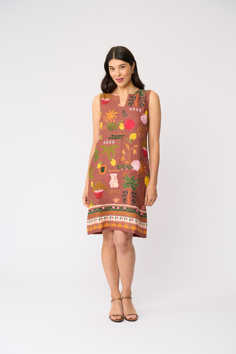 Foil clothing modeling a sleeveless brown dress with a colorful tropical and floral print, standing against a plain white studio background.
